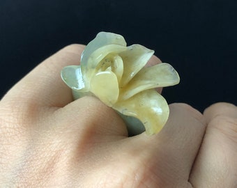 以下が含まれることがあります： 花の形をした彫刻された翡翠の指輪。花は薄い緑色で、繊細で複雑なデザインをしています。