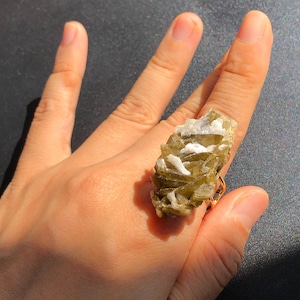 May include: A gold ring with a large, green and white crystal stone. The stone is a cluster of many smaller crystals.