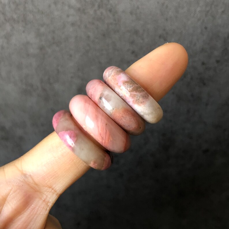 Pode incluir: Quatro an&eacute;is empilhados feitos de pedra com padr&otilde;es rosa e branco. Os an&eacute;is s&atilde;o lisos e polidos.