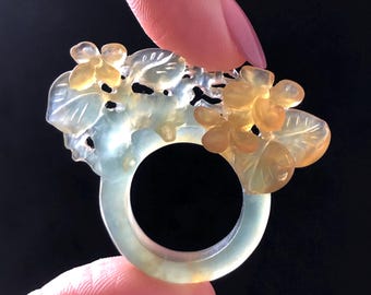 以下が含まれることがあります： 花柄が彫刻された翡翠の指輪。指輪は緑と黄色で、繊細な葉と花が特徴です。