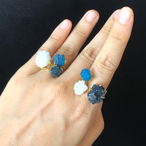 May include: Three gold rings with different colored crystal stones. The rings feature a white, blue, and black crystal stone.