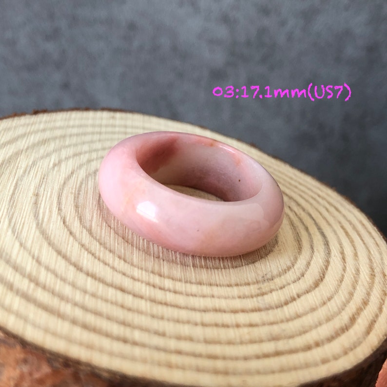 Pode incluir: Um anel de pedra preciosa rosa com um acabamento liso e polido. O anel tem um tamanho de 17,1 mm, o que corresponde a um tamanho 7 dos EUA.