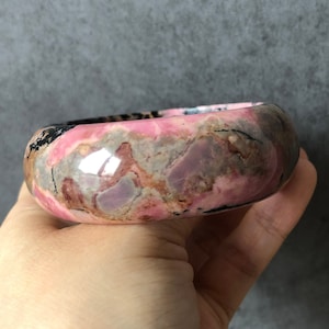 May include: A pink and gray gemstone bangle bracelet with black veins. The bracelet is polished and has a smooth surface.