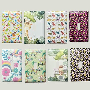 May include: A collection of eight decorative light switch covers. Designs include colorful dinosaurs, a giraffe in a jungle scene, a pink leopard print, and a unicorn with a rainbow. The covers are rectangular with a single switch opening.