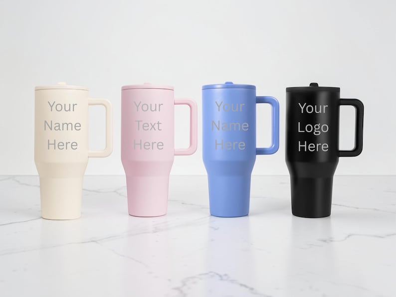 Puede incluir: Cuatro vasos aislados con asas y tapas en crema, rosa, azul y negro. Cada vaso tiene el texto "Your Name Here", "Your Text Here" o "Your Logo Here" en fuente plateada. Los vasos est&aacute;n sobre una superficie blanca.