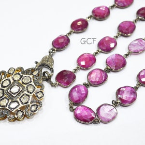Puede incluir: Un collar largo de cadena plateada con un colgante que presenta un grupo de pequeños diamantes engastados en oro. La cadena está hecha de cuentas de piedras preciosas rosadas.