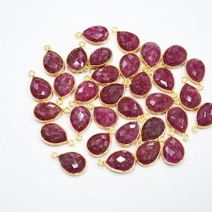 Peut inclure: Une collection de pendentifs en forme de goutte de rubis avec des montures dorées. Les pierres précieuses à facettes sont d'un rouge-violet profond. Chaque pendentif a une petite boucle en haut pour l'attacher à une chaîne ou à un autre composant de bijou.