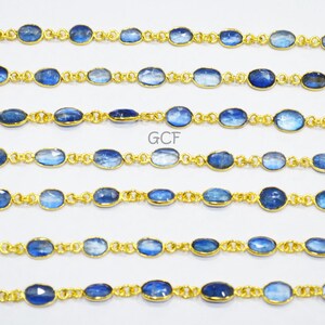 May include: A strand of blue kyanite gemstone beads with gold-toned metal connectors. The beads are oval-shaped and have a slightly iridescent finish. The strand is approximately 18 inches long.