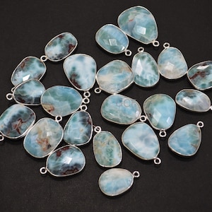 Puede incluir: Una colección de 18 colgantes de piedra preciosa azul y verde con conectores de baíl de plata. Las piedras tienen una forma irregular y una apariencia nublada y veteada.