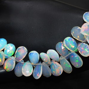 May include: A strand of iridescent white opal gemstone beads in a teardrop shape. The beads are strung on a clear thread and are arranged in a curved line.