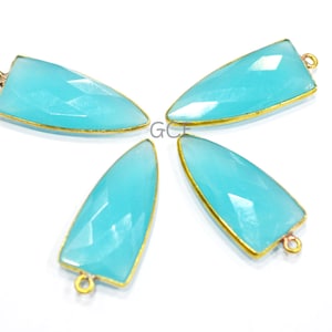 Puede incluir: Cuatro colgantes de piedra preciosa azul claro con detalles en metal dorado. Cada colgante tiene forma de lágrima con una punta puntiaguda. Los colgantes están dispuestos en forma de estrella.