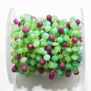 Op de afbeelding: Een groene en roze edelsteen rozenkransketting met gouden accenten. De ketting is op een spoel gewikkeld.
