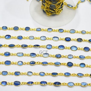 May include: A gold chain with oval-shaped blue gemstones. The chain is laid out in rows on a white surface.