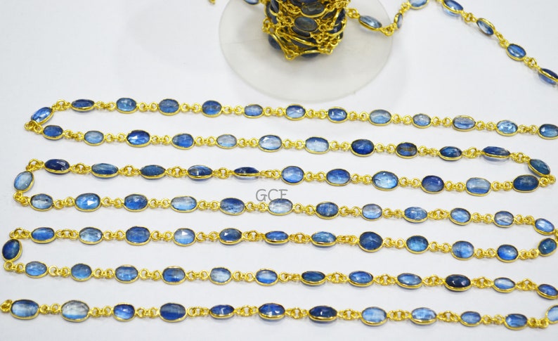 May include: A gold chain with oval-shaped blue gemstones. The chain is laid out in rows on a white surface.
