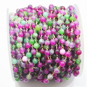 May include: A spool of pink, green, and purple gemstone beads strung on a gold chain. The beads are round and have a smooth, polished finish.