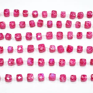May include: Rows of faceted, rectangular, hot pink gemstones strung on silver chains. The gemstones are evenly spaced and appear to be of varying sizes. The background is a plain white surface. This image showcases jewelry components.