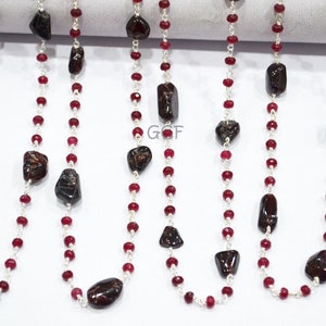 May include: A silver chain necklace with red beads and dark brown gemstone accents. The necklace is approximately 18 inches long.