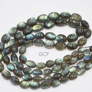 May include: A strand of oval-shaped labradorite gemstone beads in shades of gray, green, and blue. The beads are strung on a clear elastic cord.