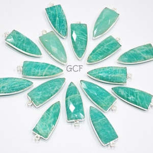 May include: A collection of 15 green aventurine arrowhead pendants with silver-toned bail settings. The pendants are arranged in a circular pattern on a white background.