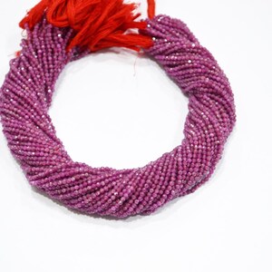Può includere: Un filo di piccole perline rosa intenso sfaccettate. Le perline sono strettamente infilate insieme, formando una forma a corda attorcigliata. Un fascio di nappe rosse è attaccato a un'estremità. Le perline sono su sfondo bianco.