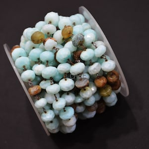 May include: A close-up of a strand of light blue and brown gemstone beads strung on a copper chain. The beads are faceted and have a natural, irregular shape.