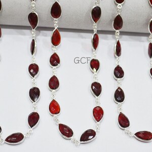 Puede incluir: Una cadena de plata con cuentas de piedra roja en forma de lágrima. La cadena está hecha de pequeños eslabones de plata y las cuentas son facetadas y tienen un color rojo intenso.