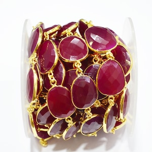 May include: A close-up of a gold chain with red gemstone beads. The chain is coiled up and the beads are faceted. The chain is perfect for jewelry making.