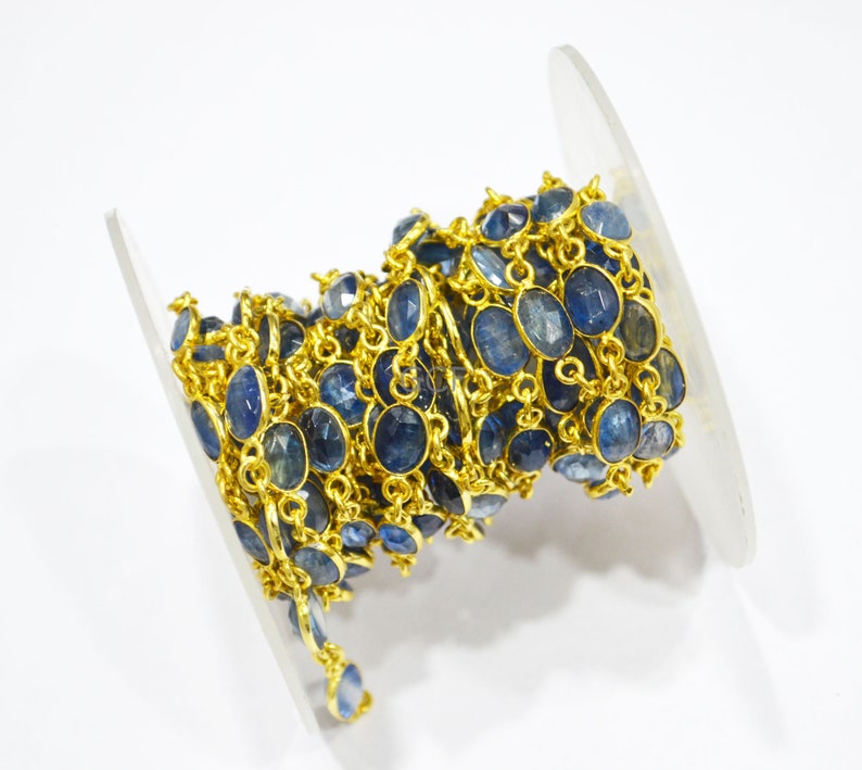 May include: A gold chain with blue gemstone beads. The chain is coiled on a white spool.