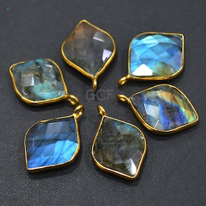 May include: Six iridescent blue labradorite gemstone pendants with gold-toned metal settings. The pendants are shaped like a teardrop with a pointed tip and a rounded base.