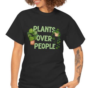 Könnte beinhalten: Schwarzes T-Shirt mit dem grünen Text "PLANTS OVER PEOPLE". Das Shirt zeigt eine Grafik von Topfpflanzen. Das Model trägt eine blaue Jeans. Das Shirt besteht aus einem weichen, bequemen Material.