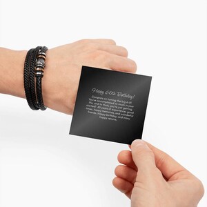 May include: A black leather bracelet with silver and copper accents is wrapped around a wrist. A black card with the text "Happy 60th Birthday!" is held in the hand.