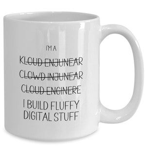 Peut inclure: Une tasse à café en céramique blanche avec du texte noir qui dit "Je suis un ingénieur Cloud Je construis du contenu numérique moelleux". Le mot "Ingénieur" est barré et le mot "Ingénieur" est écrit en dessous.