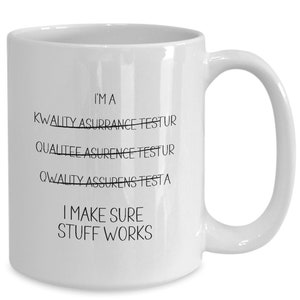 May include: White ceramic coffee mug with black text that reads "I'MA KWALITY ASURRANCE TESTUR QUALITEE ASURENCE TESTUR QWALITY ASSURENS TESTA I MAKE SURE STUFF WORKS"