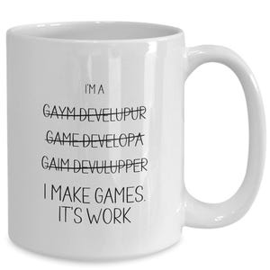Peut inclure: Mug en céramique blanche avec une anse incurvée. Le mug présente un texte noir qui se lit comme suit : "I'M A GAYM DEVELUPUR GAME DEVELOPA GAIM DEVULUPPER I MAKE GAMES. IT'S WORK."