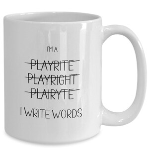 May include: White ceramic mug with a curved handle. The mug features the text "I'M A" above the crossed-out words "PLAYRITE", "PLAYRIGHT", and "PLAIRYTE". Below, it reads "I WRITE WORDS" in black, simple font.