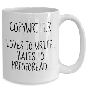 May include: White ceramic coffee mug with black text that reads "COPYWRITER LOVES TO WRITE. HATES TO PROOFREAD."