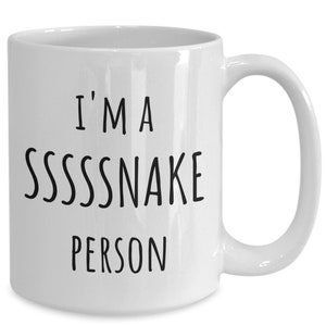 Peut inclure: Une tasse à café en céramique blanche avec du texte noir qui dit "I'm a SSSSSNAKE PERSON".