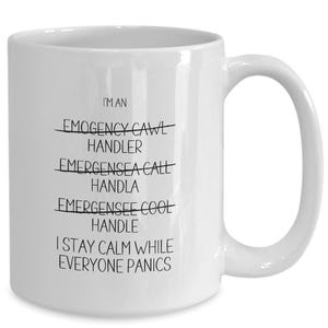 May include: White ceramic coffee mug with black text that reads "I'm an Emergency Call Handler" with the word "Emergency" crossed out and the word "Call" crossed out. The text continues with "I stay calm while everyone panics."