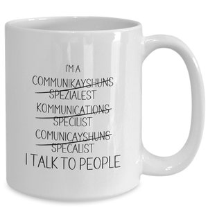 Peut inclure: Une tasse à café en céramique blanche avec du texte noir qui dit "Je suis un CommuniKAYSHUNS Spezialest, Kommunications Specilist, CommuniKAYSHUNS Specalist, I TALK TO PEOPLE".