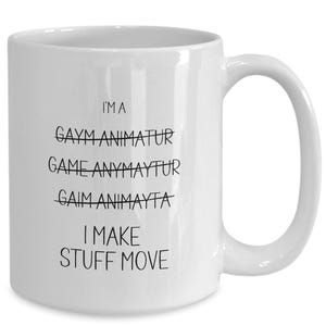 May include: White ceramic mug with a curved handle. The mug features black text that reads "I'M A GAYM ANIMATUR GAME ANYMAYTUR I MAKE STUFF MOVE". The word "GAIM ANIMAYTA" is crossed out.
