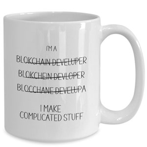 May include: White ceramic coffee mug with black text that reads "I'm a Blockchain Developer" with the word "Developer" crossed out and replaced with "Develupa". The text below reads "I make complicated stuff".