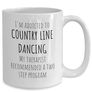 May include: White ceramic coffee mug with black text that reads "I'm addicted to country line dancing. My therapist recommended a two step program."