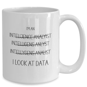 May include: White ceramic coffee mug with black text that reads "I'm an Intelligence Analyst" with the "Intelligence" crossed out and the text "I look at data" below.