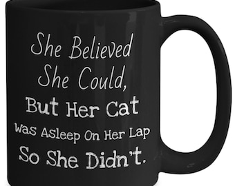 May include: Black coffee mug with white text that reads "She Believed She Could, But Her Cat Was Asleep On Her Lap So She Didn't."