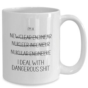 May include: White ceramic coffee mug with black text that reads "I'm a Nuclear Engineer I deal with dangerous shit". The word "Nuclear" is crossed out and the words "Newclear" and "Nukular" are crossed out above it.