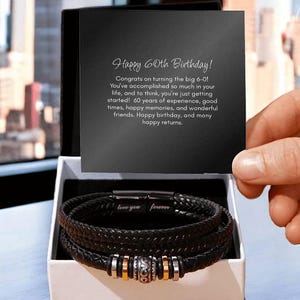 May include: A black leather bracelet with silver and gold accents, presented in a gift box. The bracelet has the words "love you forever" engraved on it. A card inside the box reads "Happy 60th Birthday!"