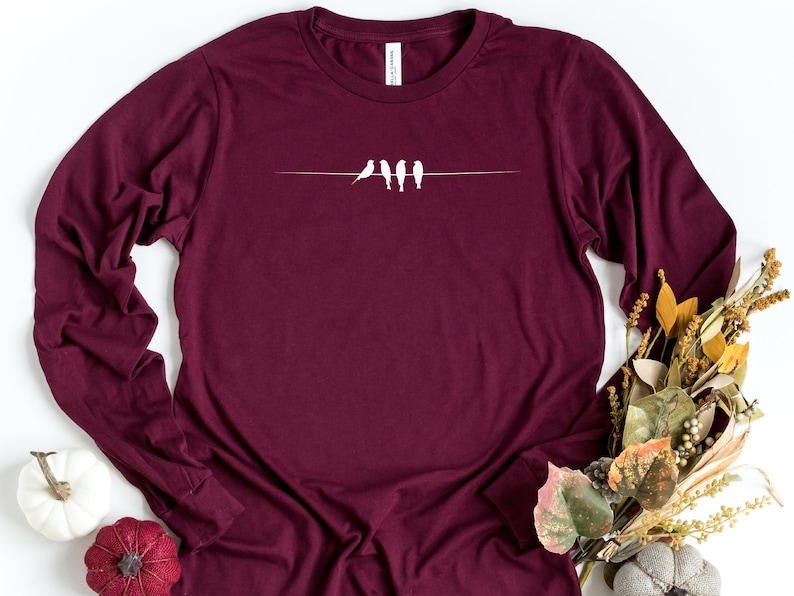 May include: A maroon long-sleeved t-shirt with a white silhouette of four birds perched on a wire.