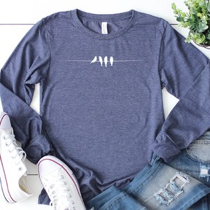 May include: A navy blue long-sleeved shirt with a white graphic of five birds perched on a wire.