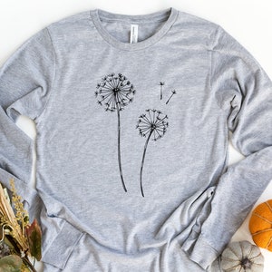 May include: A grey long-sleeved t-shirt with a black graphic of two dandelions. The dandelions are drawn in a simple, minimalist style.