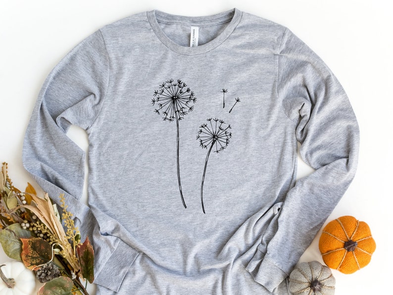 May include: A grey long-sleeved t-shirt with a black graphic of two dandelions. The dandelions are drawn in a simple, minimalist style.